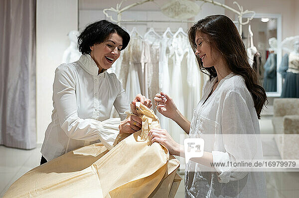 Fröhliche Ladenbesitzerin packt Kleider ein und spricht mit einer zufriedenen Kundin