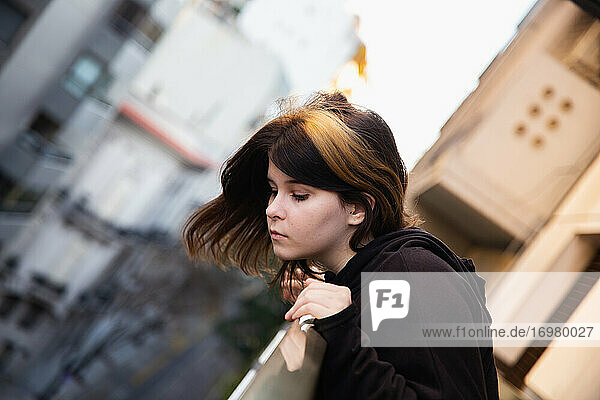 Cute teen girl looks down from the balcony of a city building