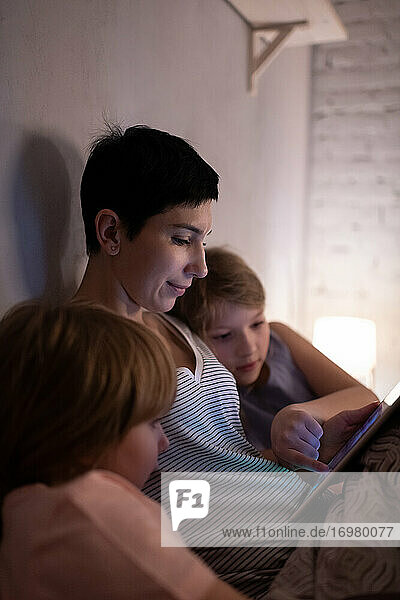 Mutter und Töchter benutzen abends gemeinsam ein Tablet
