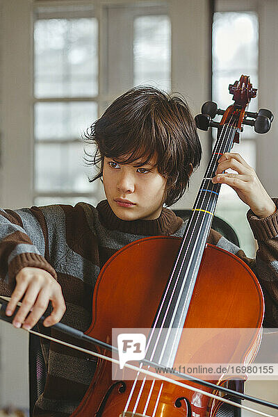 Nahaufnahme eines Jungen im Teenageralter mit ernstem Gesichtsausdruck  der zu Hause Cello spielt