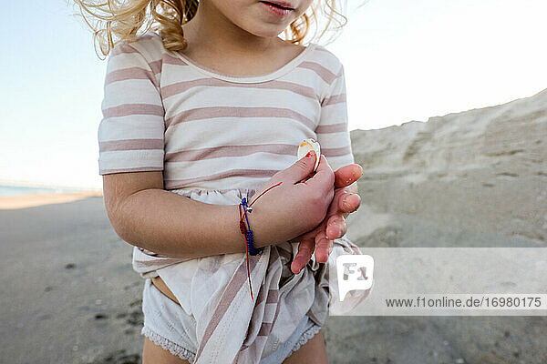 detail shot of little girl holding shells on the beach with dress on