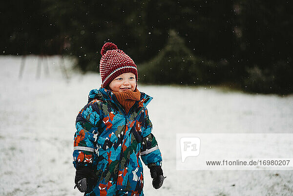 Beautiful boy smiling outside in park on cold snowy day in winter