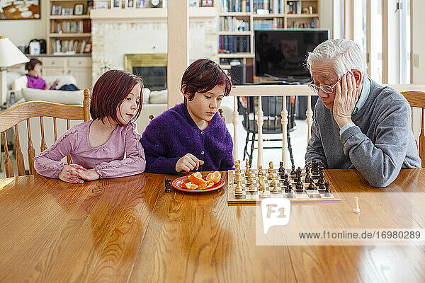 Zwei Kinder spielen Schach mit Großvater und Frau liest im Hintergrund
