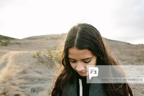 Tween Girl Looks Down While Standing In Sunlight While Out On A Hike