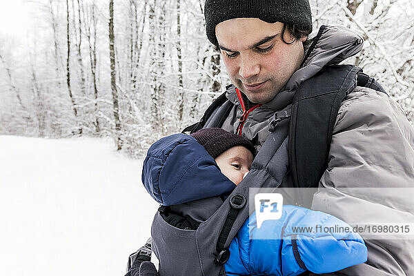 Father with adorable baby in carrier standing in snowy winter woods
