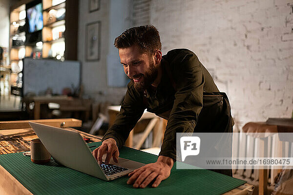 Fröhlicher Kunsthandwerker mit Laptop im Atelier