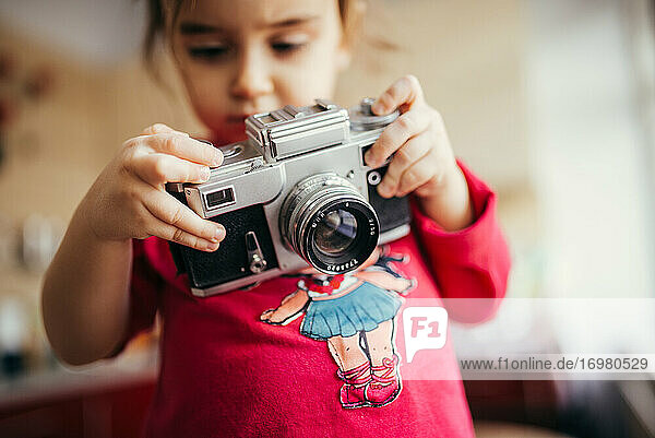 Kleines Mädchen  das eine analoge Kamera hält und einstellt.