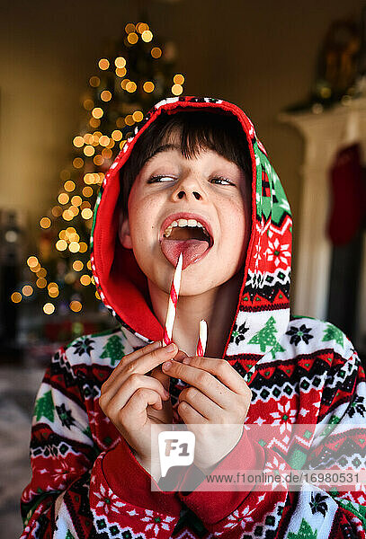 Süßer Junge im festlichen Pyjama  der zur Weihnachtszeit eine Zuckerstange isst.