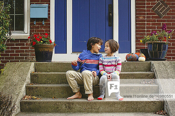 Ein Bruder und eine Schwester sitzen lächelnd auf der Eingangstreppe ihres Hauses