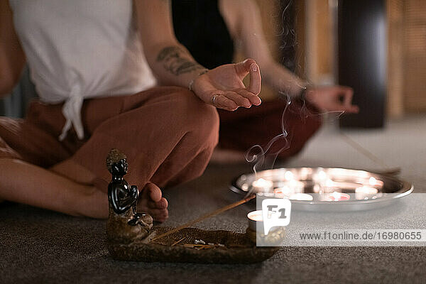 Abgeschnittene Frau meditiert neben Weihrauch und Kerzen
