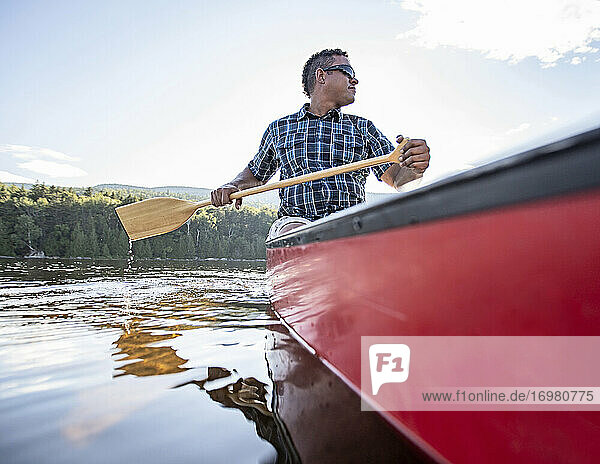 Afroamerikanischer Mann paddelt mit einem roten Kanu auf einem friedlichen See in Maine