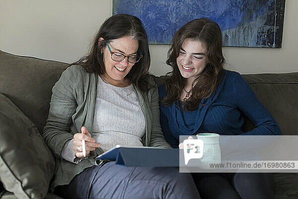 Eine Mutter und ihre Tochter lächeln  während sie gemeinsam auf ein Tablet schauen