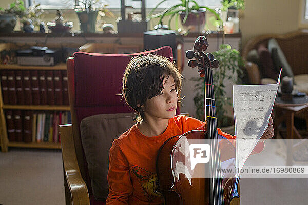 Ein Junge sitzt in schönem Licht mit einem Cello und liest Noten