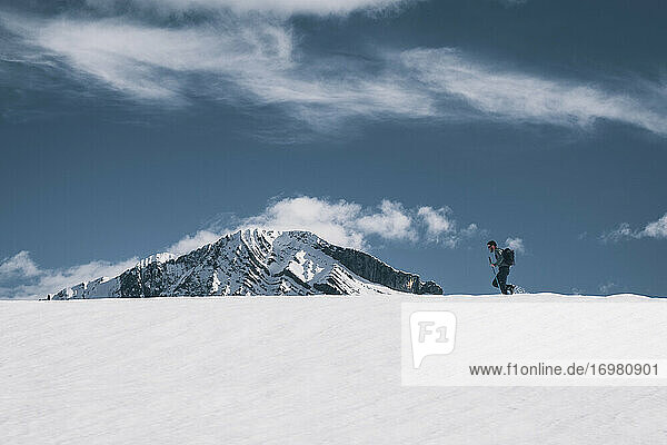 Junger Mann wandert auf einem verschneiten Bergrücken gegen einen schneebedeckten Gipfel