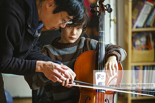 Ein Kind  das ein Cello in der Hand hält  lernt von seinem Vater  wie man den Bogen richtig hält