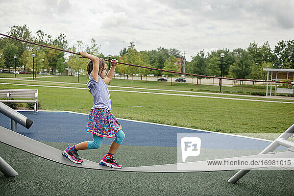 Ein kleines Mädchen balanciert im Sommer draußen auf einem Spielplatzgerät
