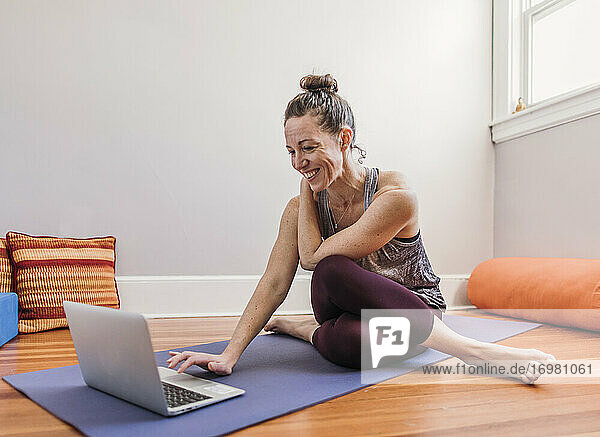 Lächelnde Frau in Yogakleidung trainiert mit Laptop in ihrem Haus