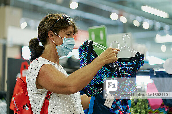 Frau mit medizinischer Maske bei der Kleiderauswahl in einem Einkaufszentrum