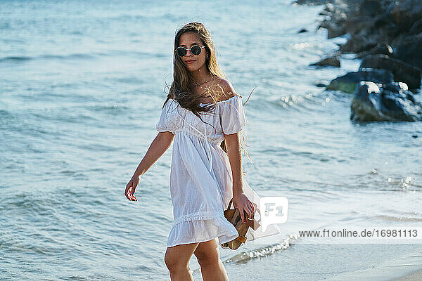 Junge Frau mit Sonnenbrille und weißem Kleid geht spazieren