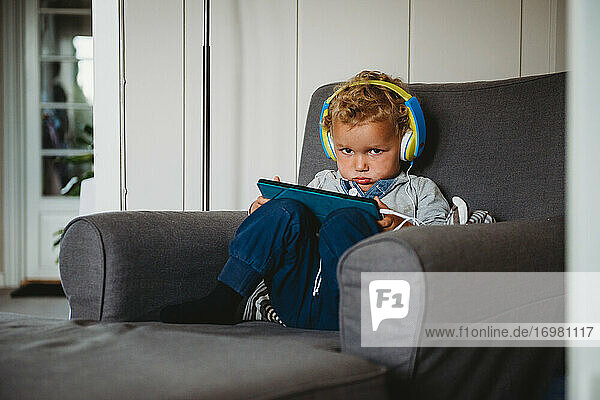 Junge schmollt  spielt mit einem Tablet und trägt Kopfhörer zu Hause covid