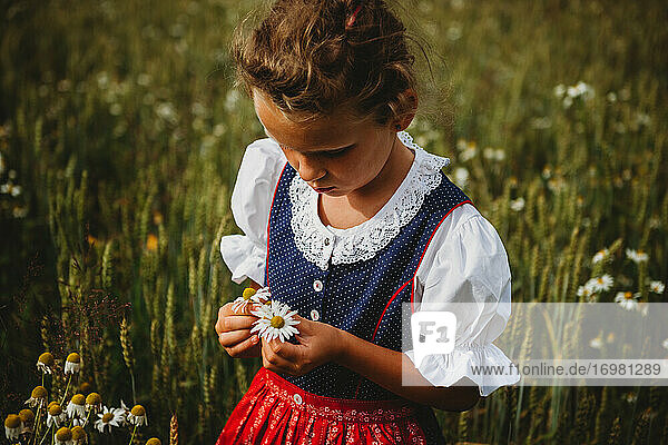 Schönes Mädchen sammelt Blumen auf dem Feld und trägt ein deutsches Dirndl