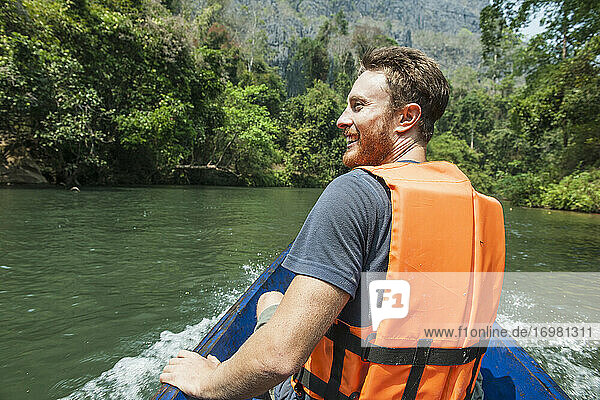 Junger Mann genießt eine Fahrt auf einem Longtailboot in Laos