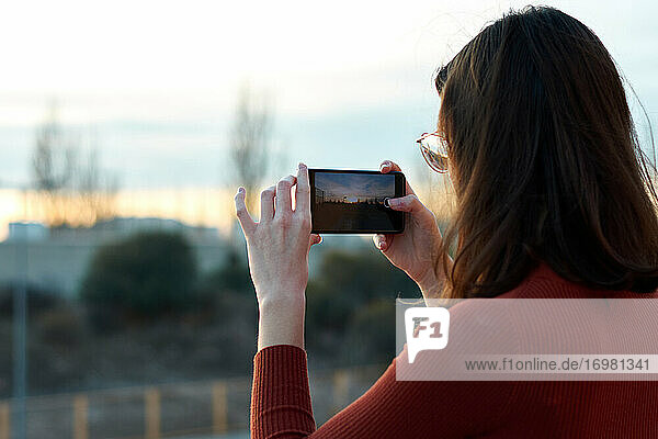 Junge Frau macht ein Foto mit ihrem Handy bei Sonnenuntergang