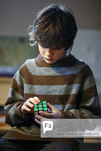 Ein kleiner Junge im übergroßen Pullover löst geduldig einen Rubik's Cube