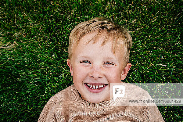Glücklicher Junge liegt lächelnd im Gras