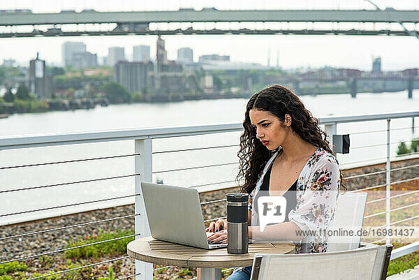 Woman working on laptop at small table outside on roof