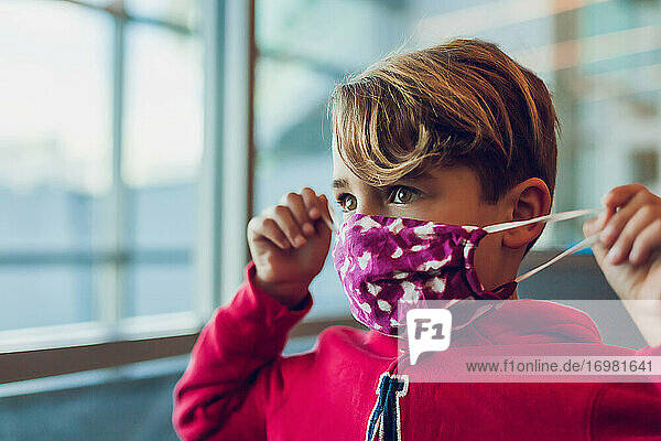 Young boy wearing a mask close to a window at airport  fixes own mask.