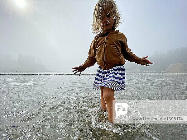 Ein junges Mädchen spielt an einem nebligen Tag an der Küste von OR im Meer.