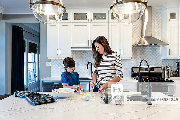 Mutter und Sohn backen gemeinsam Muffins in einer modernen weißen Küche.