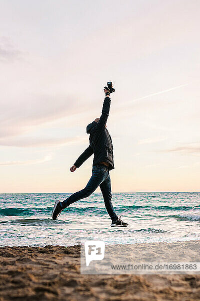 Man Jumping On The Shore Of A Beach With His Camera