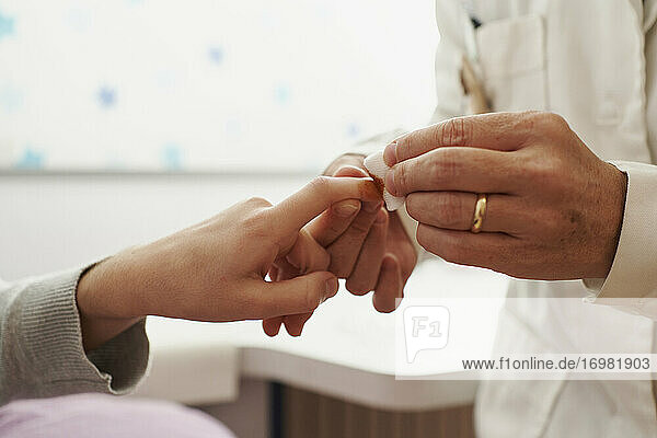 Nahaufnahme einer Ärztin  die einem Mädchen im Bett ein Pflaster auf den Finger klebt. Hausarzt-Konzept