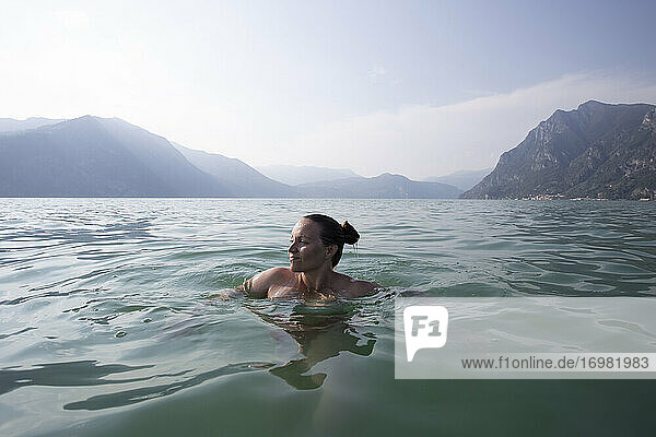 Eine junge Frau  die in der Mitte eines Sees in Italien schwimmt