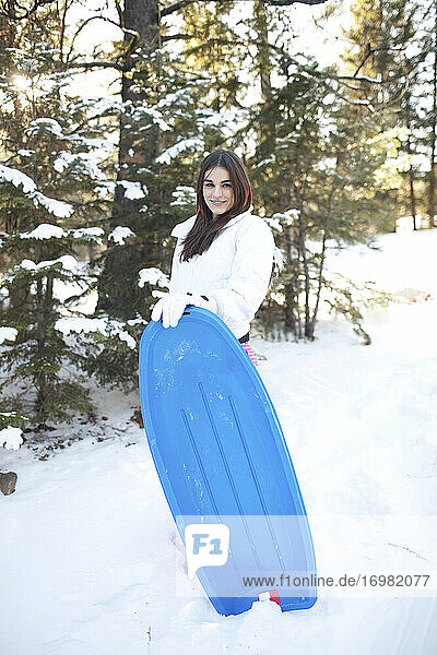 Frau hält einen blauen Schlitten im verschneiten Wald