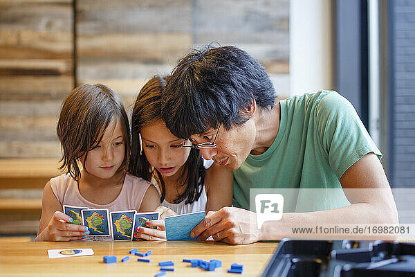 Ein Vater spielt ein Brettspiel mit seinen Töchtern an einem Holztisch