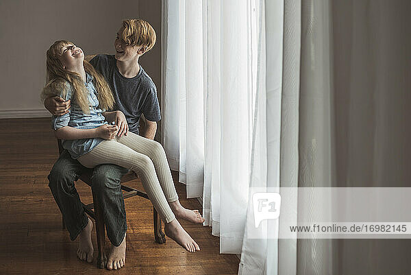 Siblings sitting on chair and laughing in natural light studio