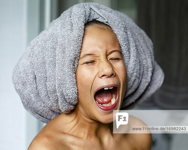 Ein Kind mit Badetuch auf dem Kopf schreit spielerisch mit weit geöffnetem Mund