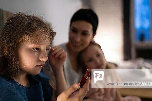 Girl applying makeup near mother and sister