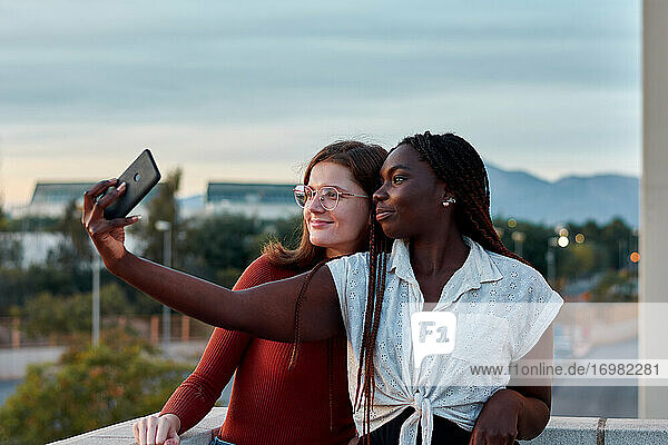 Zwei junge Frauen machen ein Selbstporträt mit ihrem Handy bei Sonnenuntergang