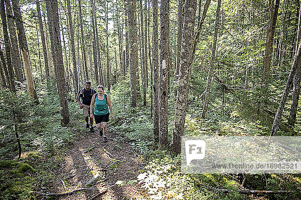 Black man and white woman hike in woods on Appalachian Trail in Maine