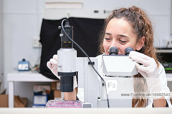 Junge Wissenschaftlerin schaut durch ein Mikroskop in einem Labor. Laborforschung Konzept.