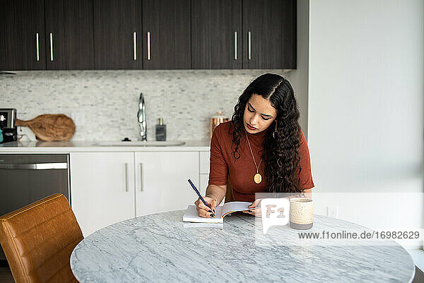 Frau schreibt in Notizbuch am Tisch mit Kaffeetasse