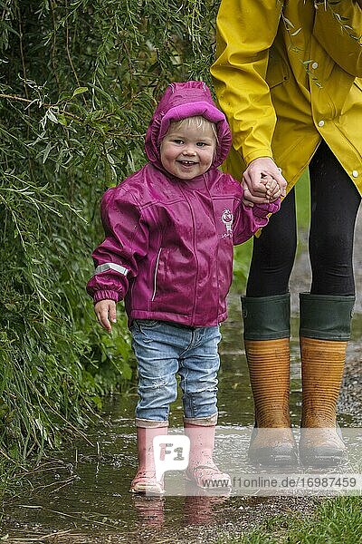 Little girl with rubber boots and rain jacket holding her mother's hand in the rain  in bad weather  Upper Bavaria  Bavaria  Germany  Europe