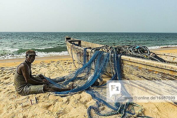 Man fixing his nets in his fishing boats on a beach in Robertsport  Liberia  Africa