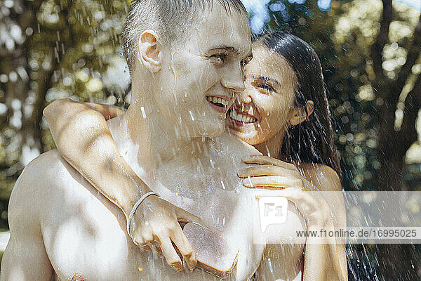 Glückliches junges Paar mit Seife duschen im Freien