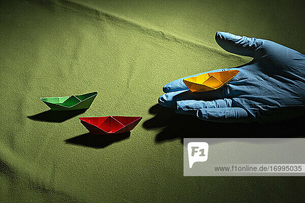 Hand im Schutzhandschuh hält Origami-Boot
