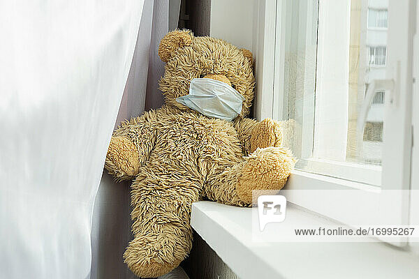 Teddybär mit Gesichtsmaske auf der Fensterbank